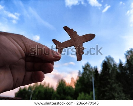 Hand holding toy wooden airplane plane and blue sky with forest background. The concept of flying on airplane, travel, leisure, adventure. Blurred picture, partial focus