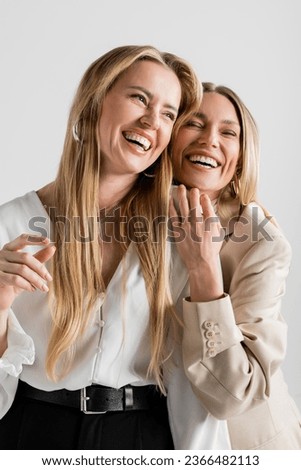 portrait of two elegant attractive sisters laughing posing on grey backdrop, bonding, fashion Royalty-Free Stock Photo #2366482113