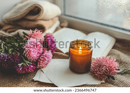 Burning candle, flowers, open book, cozy autumn.