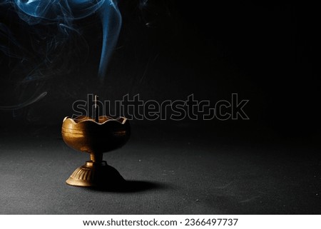 Isolated incense holder with incense sticks shiny brass or yellow colored incense vase or incense burner with black background ,used during meditation ,religious practice, smoke on dark background.