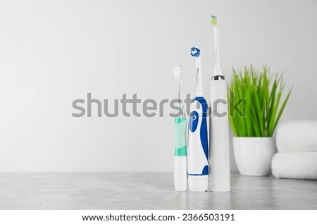 Electric toothbrushes on light grey marble table near white wall. Space for text