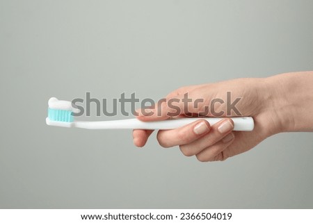 Woman holding toothbrush with paste on light grey background, closeup Royalty-Free Stock Photo #2366504019