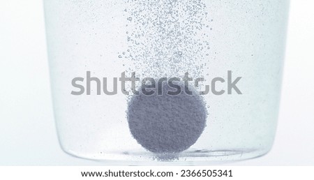 Tablets Falling and Dissolving into a Glass of Water against White Background