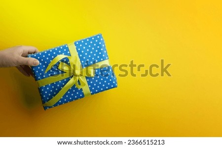 female hand are holding a blue gift box on a yellow background, happy birthday concept, copy space