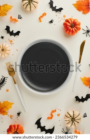 Giving life to your dining experience with Halloween magic. Top view vertical shot of cutlery, plates, pumpkins, creepy decor, autumn leaves on light grey background with advert spot