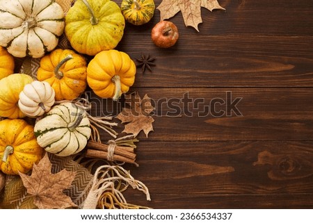 Celebrate the autumn harvest scene. Top view photo of cozy plaid, orange pumpkins, cinnamon sticks, fallen autumn leaves, anise on wooden background with promo area
