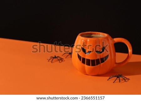 Cappuccino latte coffee in pumpkin cup on black orange background. Halloween celebration concept