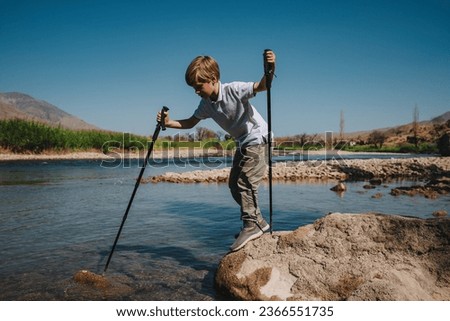 Boy with trekking poles checks the depth of mountain river