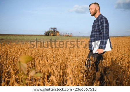 Agronomist inspecting soya bean crops growing in the farm field. Agriculture production concept. young agronomist examines soybean crop on field. Farmer on soybean field
