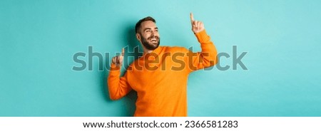 Handsome man celebrating, feeling winner, pointing fingers up and do champion dance, standing over light blue background. Royalty-Free Stock Photo #2366581283