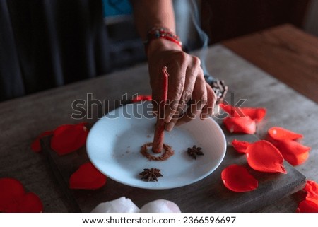 Preparation of a red candle with ground cinnamon, witch on the eve of all saints' eve performing a love ritual, Halloween, spiritual beliefs, white magic