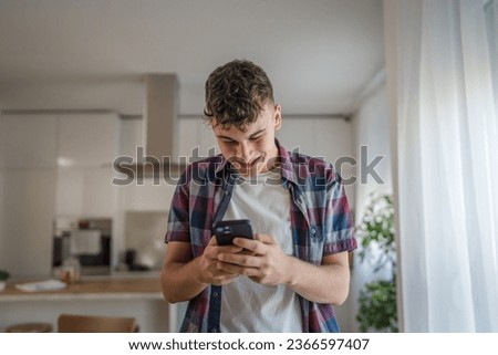 One man caucasian male teenager boy use smartphone mobile phone for online internet browsing social network or sms text messages at home happy smile