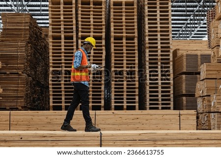 African workers man engineering walking and inspecting with working suite dress and hand glove in timber wood warehouse. Concept of smart industry worker operating. Wood factories produce wood palate.