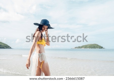 Beautiful woman in yellow bikini on tropical beach. Portrait of happy young woman smiling at sea. Brunette tanned girl in swimwear enjoying and walking on beach.