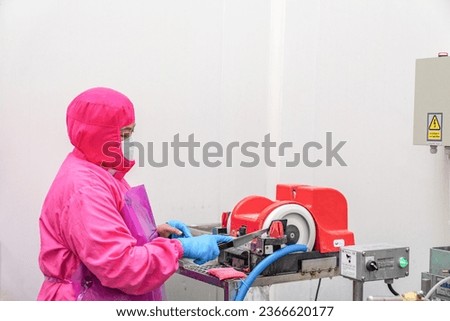 Worker sharpening the knife with a electric sharpener for cut up chicken meat parts.