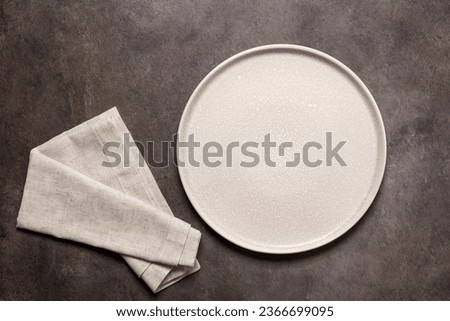 Empty beige plate with beige linen napkin on a dark brown background. Top view, flat lay. Royalty-Free Stock Photo #2366699095