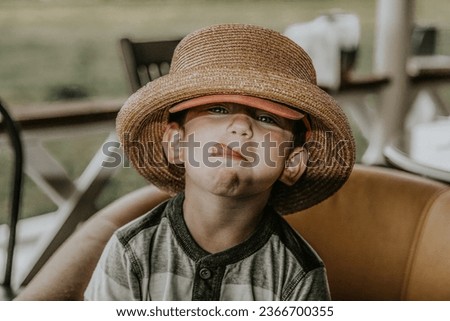 A child in a straw hat is sticking out his tongue and looking at the camera. Soft selective focus Royalty-Free Stock Photo #2366700355