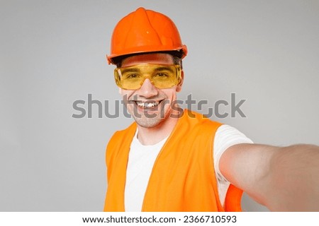 Young employee smiling handyman man in orange vest protective hardhat doing selfie shot on mobile phone isolated on grey background studio. Instruments for renovation apartment . Repair home concept