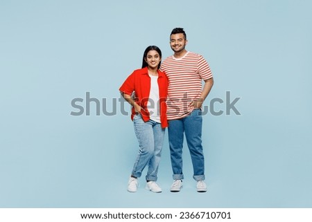 Full body satisfied happy young couple two friends family Indian man woman wear red casual clothes t-shirts together looking camera hug cuddle isolated on pastel plain light blue cyan color background