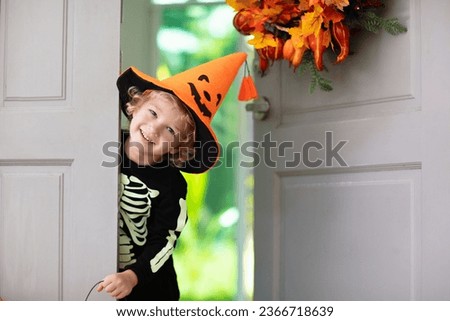 Kids trick or treat on Halloween night. Child at decorated house door with autumn leaf wreath and pumpkin lantern. Little boy in witch and skeleton costume and hat with candy bucket. Fall decoration. 