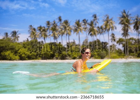 Young woman in bikini surfing on tropical beach in Asia. Girl on surf board on ocean wave. Active water sports for toned fit body. Female athlete swimming. Surfer in exotic sea. Swim and eye wear.


