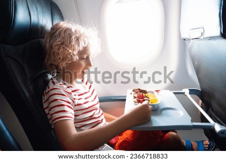 Child in airplane window seat. Kids flight meal. Children fly. Special inflight menu, food and drink for baby and kid. Boy eating healthy lunch in airplane. Travel and family vacation.   Royalty-Free Stock Photo #2366718833