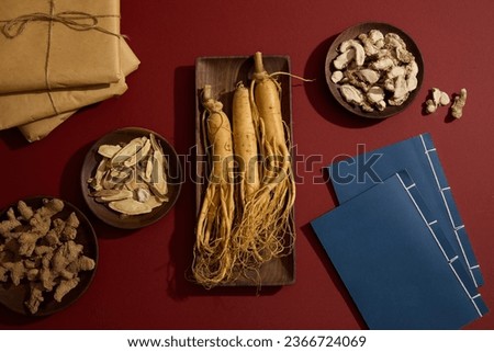 Rectangle dish of Ginseng roots displayed with round dishes of Dried turmeric, Bai zhu and Sand ginger. Two ancient Chinese medicine books and some medicine packs arranged Royalty-Free Stock Photo #2366724069