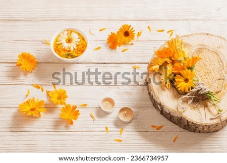Medicinal flowers of calendula with burning candles  on white wooden background