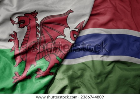 big waving national colorful flag of wales and national flag of gambia . macro