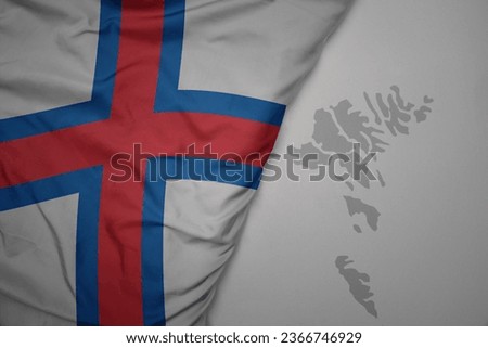big waving national colorful flag and map of faroe islands on the gray background. macro