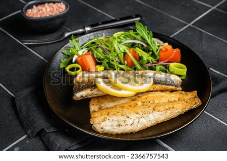 Roasted sea bass fillet with salad, Branzino fish. Black background. Top view. Royalty-Free Stock Photo #2366757543