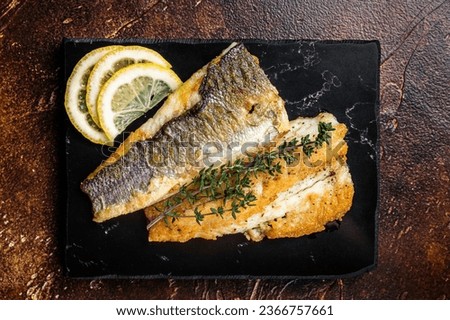 Roast sea bass fillet with lemon and thyme, seabass fish. Dark background. Top view. Royalty-Free Stock Photo #2366757661