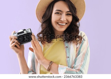 Young woman in summer hat with photo camera on lilac background, closeup