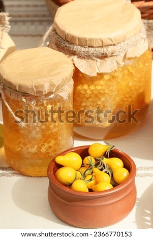 Closeup picture of two jars with fresh homemade honey and a bowl with decorative yellow peppers, outdoor shot