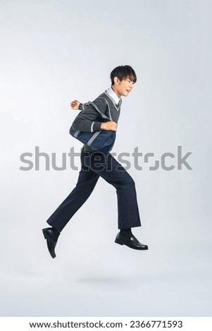 Asian male student jumping in studio with white background.
