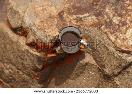 Tea in a tin mug on a rock covered with lichen