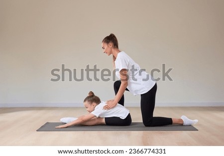 Beautiful female teacher helps a little girl stretch in a gymnastics class. The concept of education, sports, Pilates, stretching, healthy lifestyle. Mixed media