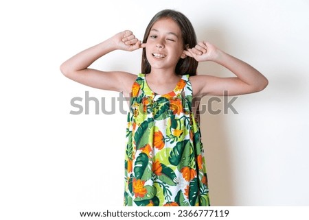 Happy young beautiful kid girl ignores loud music and plugs ears with fingers asks to turn off sound