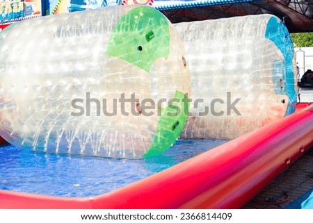 Two zorb cylinders of green and blue color on the water in an inflatable pool of an amusement park. Water attraction for children and adults.