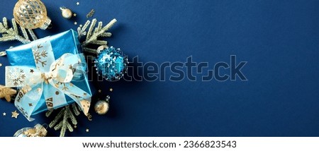 Christmas banner template. Glistering gift box with fir branches and luxury gold Xmas balls, decorations on dark blue background. Flat lay, top view, copy space.