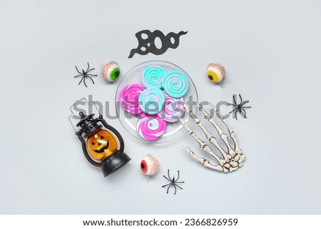 Halloween composition with sweet candies, skeleton hand and lantern on grey background