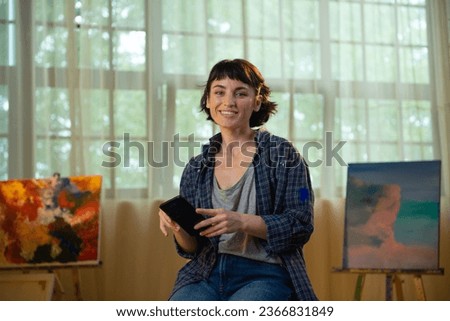 Charismatic and pretty artist woman in the studio take her smartphone and smiling large looking over and watching something