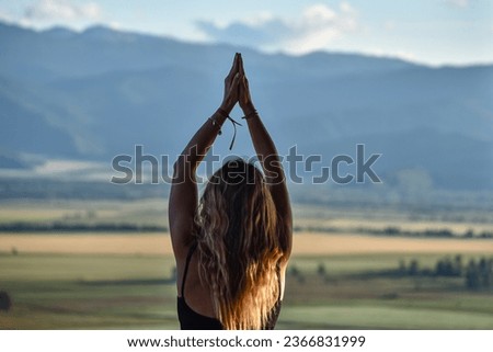 Female silhouette from backside with hands up in namaste pose with mountains background