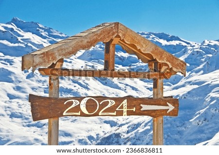 2024 written on a wooden direction sign, snowy mountain landscape on the background, ski new year card