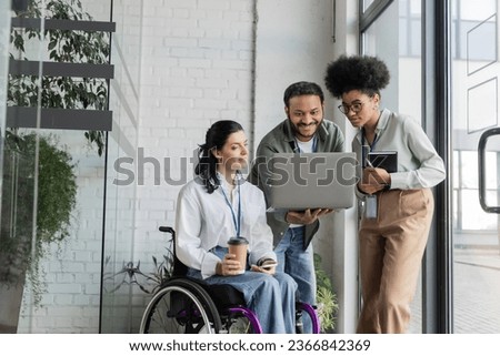 group shot of diverse business people, disabled woman on wheelchair looking at laptop with coworkers Royalty-Free Stock Photo #2366842369