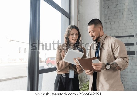 happy businesswoman showing tablet with startup project to asian colleague in modern office
