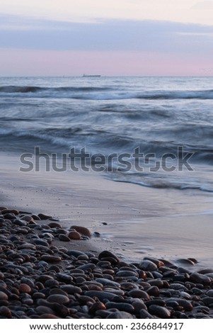 The Baltic Sea and pebbles at the light of sunset. Long exposure photo of the sea. Vertical photo.