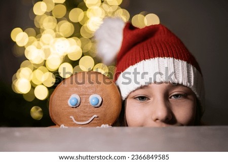 child in santa hat on christmas tree background making a gingerbread for winter holidays