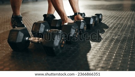Fitness, athlete and closeup of dumbbells in gym for exercise, workout and sports training. Hands of strong bodybuilder lifting heavy weights on ground in wellness club for muscle, power or challenge Royalty-Free Stock Photo #2366866351