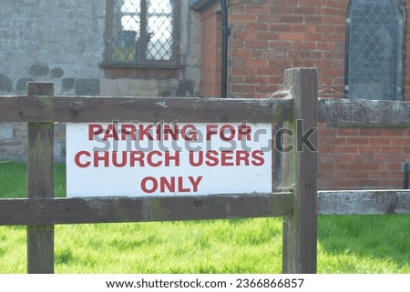 A sign on a fence stating parking for church users only. Part of the church building and windows are in the background.